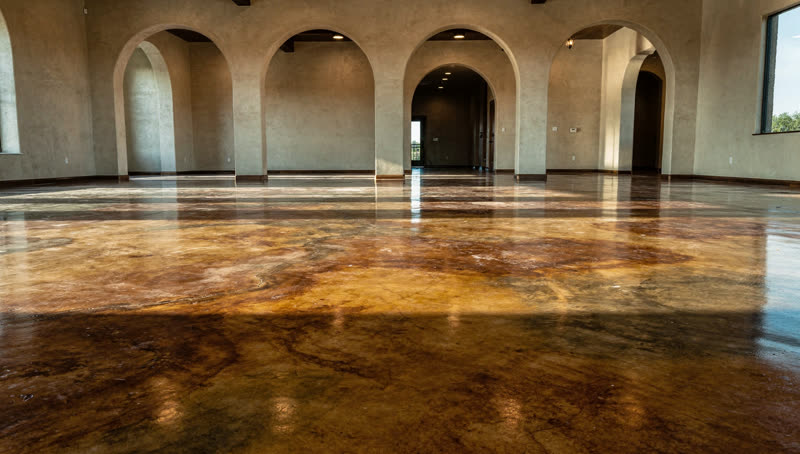 A finished commercial floor in a South Texas showroom floor with decorative acid-stained concrete in warm earth tones, arched openings, hill country light